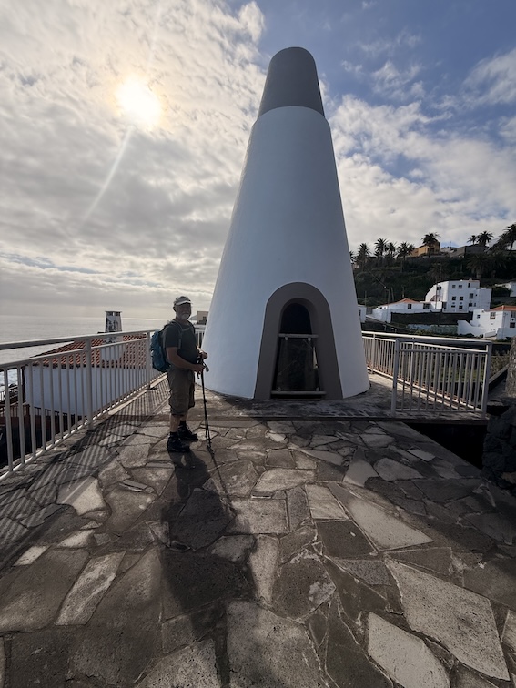Kleiner weißer Aussichtsturm an der Küste mit Wanderer und Wanderstöcken