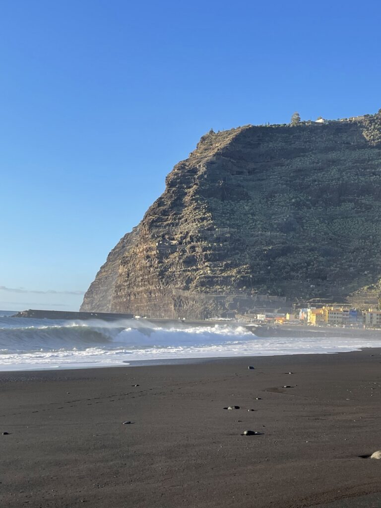 Schwarzer Sandstrand mit hohem pyramidenförmigem Steilkliff, brechenden Wellen und tiefblauem Himmel auf La Palma