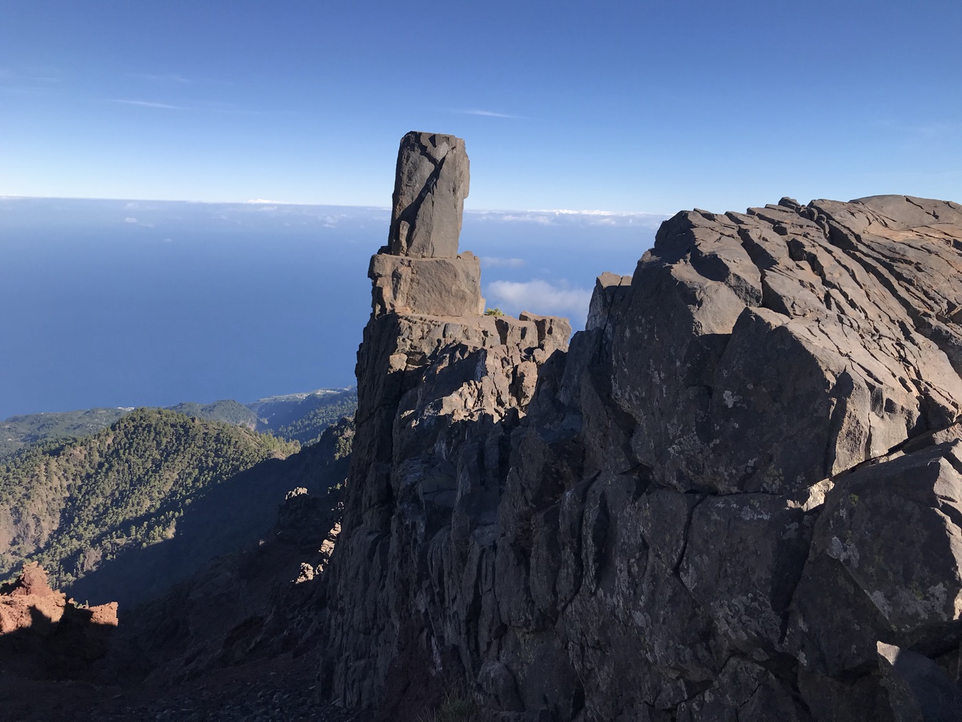 Markante Felsnadel am Gipfelgrat des Roque de los Muchachos mit Blick über Wolken zum Meer